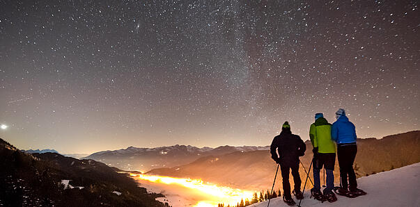 Winterwanderer genießen den Sternenhimmel über dem Weissensee in verschneiter Wintelandschaft.