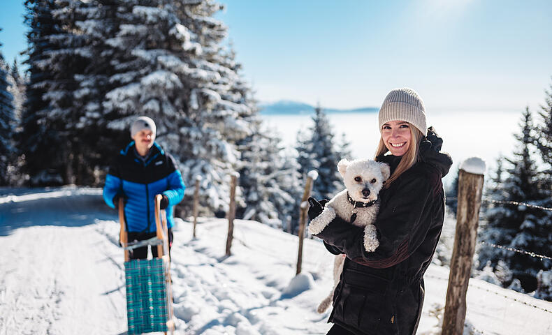 Ein Paar rodelt mit Hund auf der Saualpe im Lavanttal, Kärnten, Österreich