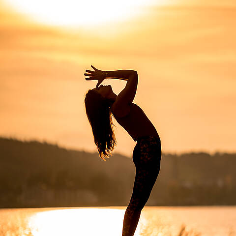 Frau macht Yogaübung beim Sonnenuntergang am Wörthersee im Herbst